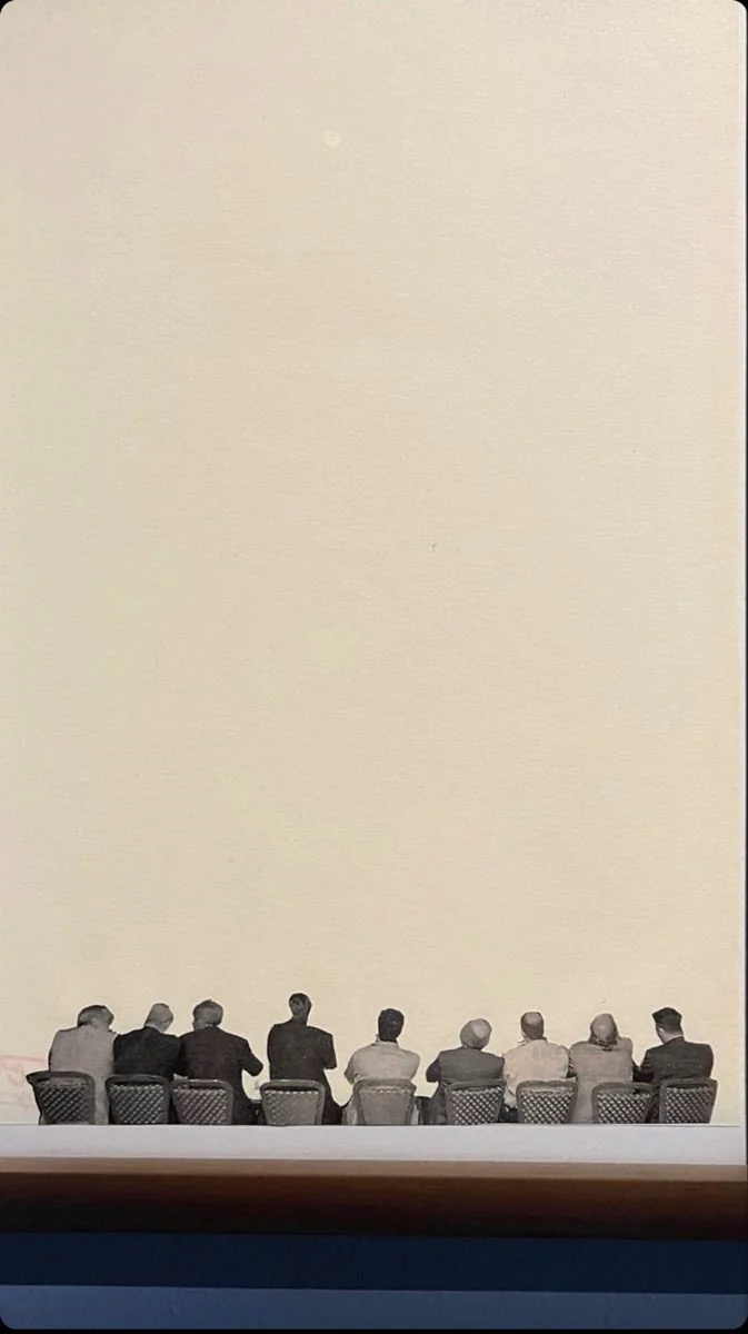 A row of people seated along one wall of a large empty room